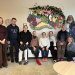 Joukko hymyileviä ihmisiä istumassa sohvalla.